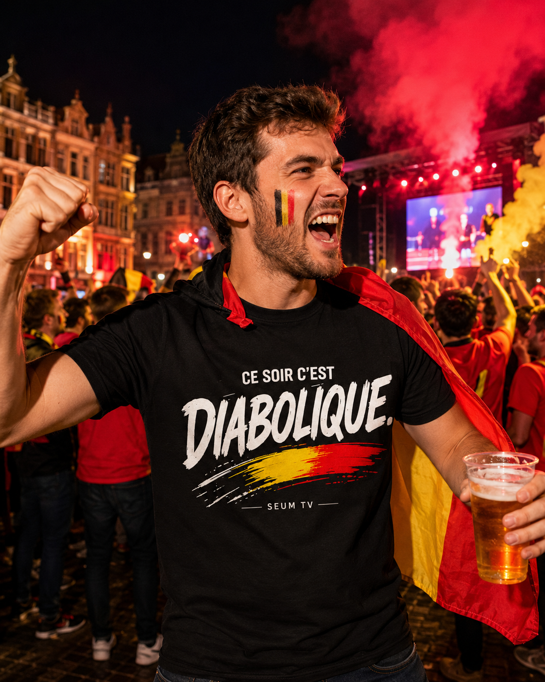 Supporter belge en t-shirt noir "Ce soir c'est Diabolique" célébrant avec ferveur, un verre à la main, dans une ambiance festive de match en plein air avec fumigènes et drapeaux.
